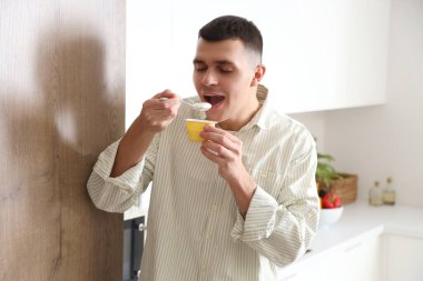 Genç adam mutfakta lezzetli yoğurt yiyor.