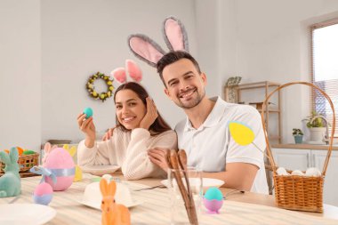Paskalya günü yemek odasında boyalı yumurtaları olan tavşan kulaklı mutlu çift.