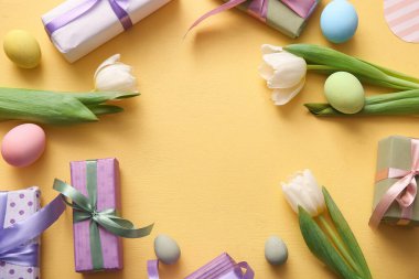 Paskalya yumurtalarından yapılmış bir çerçeve hediye kutuları ve turuncu arka planda lale çiçekleri.