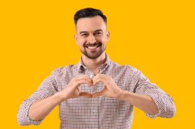 Yakışıklı adam, elleri sarı arka planda kalp yapıyor.