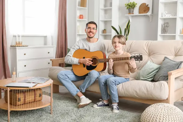 Private music teacher giving guitar lessons to little boy in living room