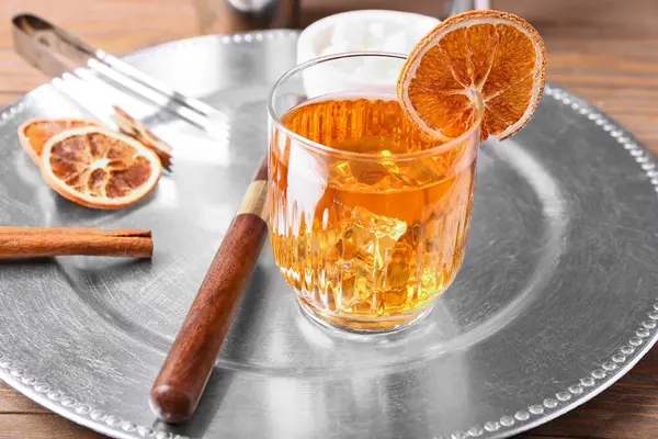Lezzetli bir bardak eski moda kokteyl ve ahşap arka planda portakal dilimleri ile metal tabak.