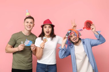 Kağıt yapıştırmalı ve pembe arka planda osuruk yastıklı komik kılık değiştirmiş genç arkadaşlar. 1 Nisan kutlamaları