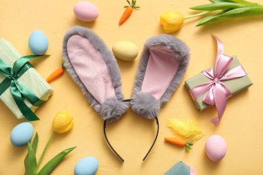 Paskalya yumurtası, havuç ve sarı arka planda hediye kutuları olan tavşan kulakları.