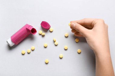 Astım spreyli bir çocuk eli ve beyaz arka planda haplar.