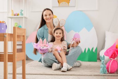 Genç anne ve küçük kızı evde Paskalya hediyesi yumurta ve pasta tutuyorlar.