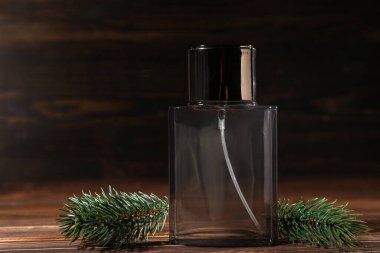 Ahşap arka planda bir şişe parfüm ve ladin dalı.