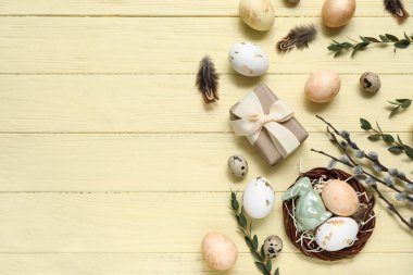 Boyanmış Paskalya yumurtaları, dalları ve sarı ahşap arka planda hediye kutusu olan bir yuva.