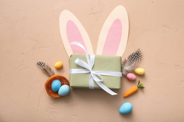 Hediye kutulu Paskalya yumurtaları, tüyler ve bej arka planda kağıt tavşan kulakları.