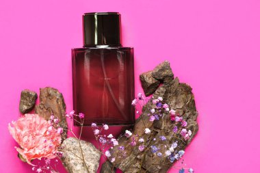 Üzerinde çingene çiçekleri ve pembe arka planda ahşap olan koyu kırmızı bir parfüm şişesi. Üst görünüm