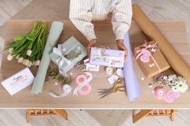 Güzel hediye kutuları olan bir kadın, tahta masada paketleme malzemeleri ve çiçekler. Uluslararası Kadınlar Günü