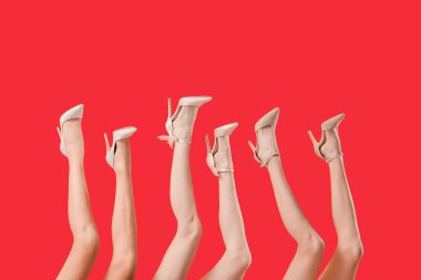 Kırmızı arka planda farklı ayakkabılar giyen kadın bacakları.