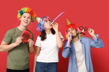 Garip kılık değiştirmiş, kırmızı arka planda düdük ve şamata yastığı olan genç arkadaşlar. 1 Nisan kutlamaları