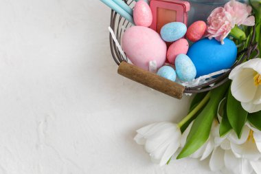 Süslü kozmetik sepetleri, Paskalya yumurtaları ve beyaz arka planda bir buket lale.