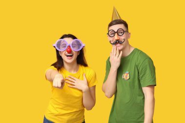 Sarı arka plandaki izleyiciye bakan kağıt balıklarıyla komik kılık değiştirmiş genç arkadaşlar. 1 Nisan kutlamaları