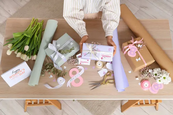 Güzel hediye kutuları olan bir kadın, tahta masada paketleme malzemeleri ve çiçekler. Uluslararası Kadınlar Günü