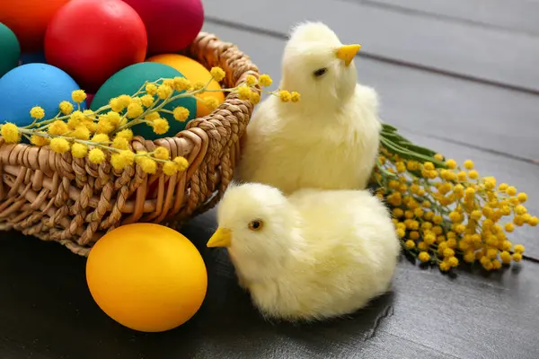 Şirin hatunlar, mimoza çiçekleri ve koyu ahşap arka planda boyanmış Paskalya yumurtaları olan sepet.