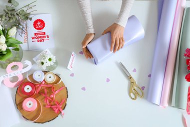 Hediye kutusu olan kadın elleri, paketleme malzemeleri ve arka planda tebrik kartları