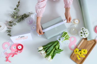 Hediye kutusu olan kadın elleri, paketleme malzemeleri ve arka planda güzel çiçekler. Uluslararası Kadınlar Günü