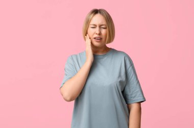 Güzel, olgun bir kadın pembe arka planda diş ağrısı çekiyor.
