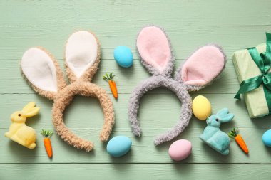 Paskalya yumurtalı tavşan kulakları, havuç ve yeşil ahşap arka planda hediye kutuları.