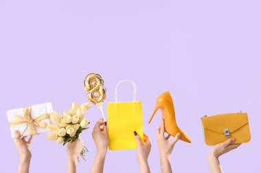 Leylak arka planında bir buket lale, el çantası ve hediye kutusu olan kadın elleri. Uluslararası Kadınlar Günü için Alışveriş