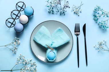 Mavi arka planda yumurta ve çiçeklerle Paskalya için güzel bir masa.