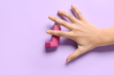 Leylak arka planında astım spreyi olan bir çocuk eli.