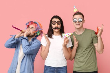 Pembe arka planda parti düdükleriyle kılık değiştirmiş genç arkadaşlar. 1 Nisan kutlamaları