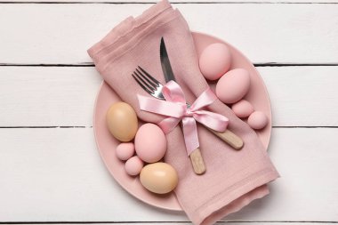 Paskalya yumurtaları, peçete ve beyaz ahşap arka planda çatal bıçak seti olan güzel bir masa.