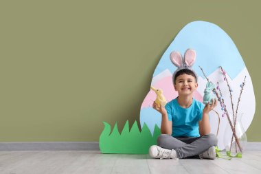 Paskalya tavşanları ve yeşil duvarın yanındaki dekorasyonlarla tavşan kulağı takan şirin bir çocuk.