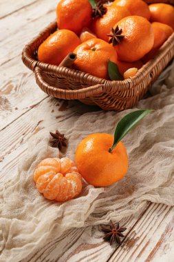 Beyaz ahşap zemin üzerinde yıldız anason ve tarçın olan sepet dolusu tatlı mandalina.