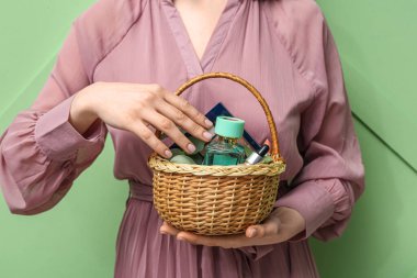 Yeşil arka planda dekoratif kozmetiklerle dolu sepeti olan güzel genç bir kadın.