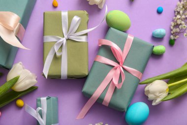 Çiçekli Paskalya yumurtaları ve mor arka planda hediye kutuları.