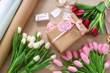 Ahşap zemin üzerinde Uluslararası Kadınlar Günü için hediye paketi, paketleme malzemeleri ve güzel lale çiçekleri olan kompozisyon