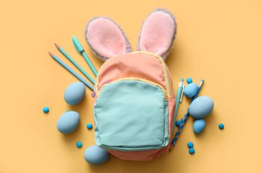 Tavşan kulaklı, Paskalya yumurtası ve sarı arka planda okul malzemeleri.