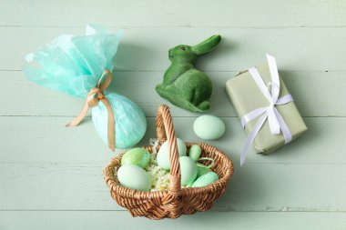 Boyanmış Paskalya yumurtaları, oyuncak tavşancık ve yeşil ahşap arka planda hediye kutusu olan hasır sepet.