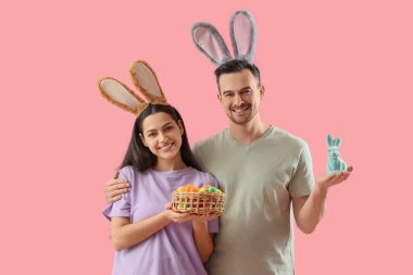 Paskalya tavşanı ve pembe arka planda yumurtaları olan tavşan kulaklı mutlu çift.
