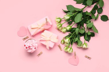 Hediyeler, taze güller ve pembe arka planda kek.