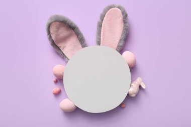 Paskalya yumurtalı tavşan kulakları ve leylak arkaplanlı boş tebrik kartı.