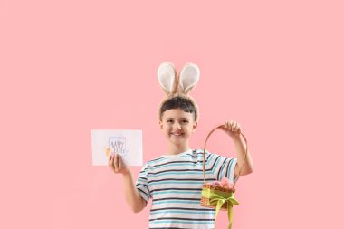Paskalya hediyesi kartı ve pembe arka planda sepeti olan tavşan kulaklı şirin bir çocuk.