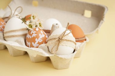 Süslü Paskalya yumurtaları ve bej arka planda küçük çiçekler olan karton kutu.