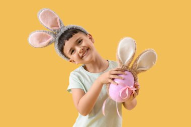 Paskalya hediyesi yumurtası ve sarı arka planda tavşan kulağı olan şirin bir çocuk.