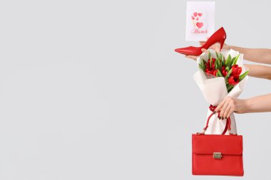 Kırmızı lale buketi, el çantası ve beyaz arka planda neşeli kartpostalları olan kadın elleri. Uluslararası Kadınlar Günü için Alışveriş