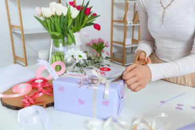 Işık masasında güzel çiçeklerle hediye paketi hazırlayan bir kadın. Uluslararası Kadınlar Günü
