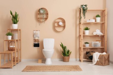 Ev bitkilerinin ve bej duvarın yanında seramik klozetin bulunduğu şık bir banyo.