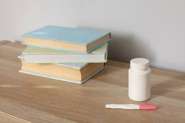 Pregnancy test with pill bottle and books on shelf in room