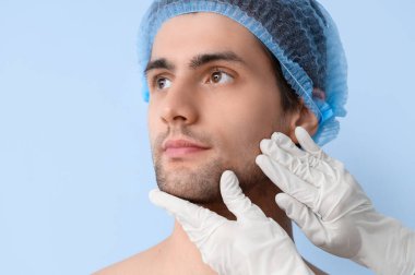Mavi arka planda estetik cerrahı olan yakışıklı genç adam, yakın plan.