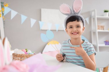 Evdeki kağıt yumurtaları işaret eden tavşan kulaklı şirin bir çocuk. Paskalya kutlaması