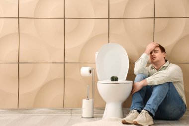 Genç adam ve tuvalette kaktüs olan klozet. Hemoroit konsepti